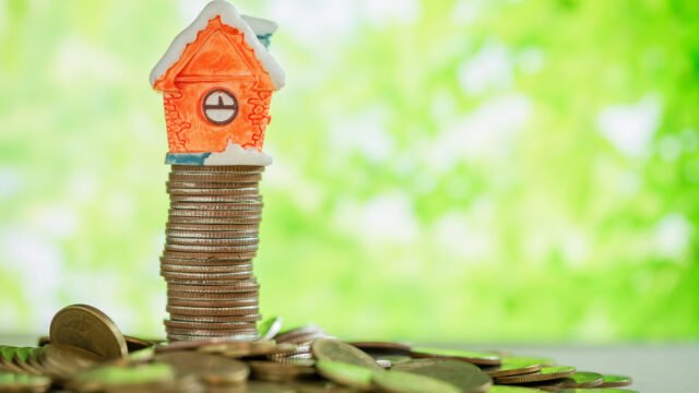 Mini house on a tall stack of coins showing property investment stability and long-term wealth growth.