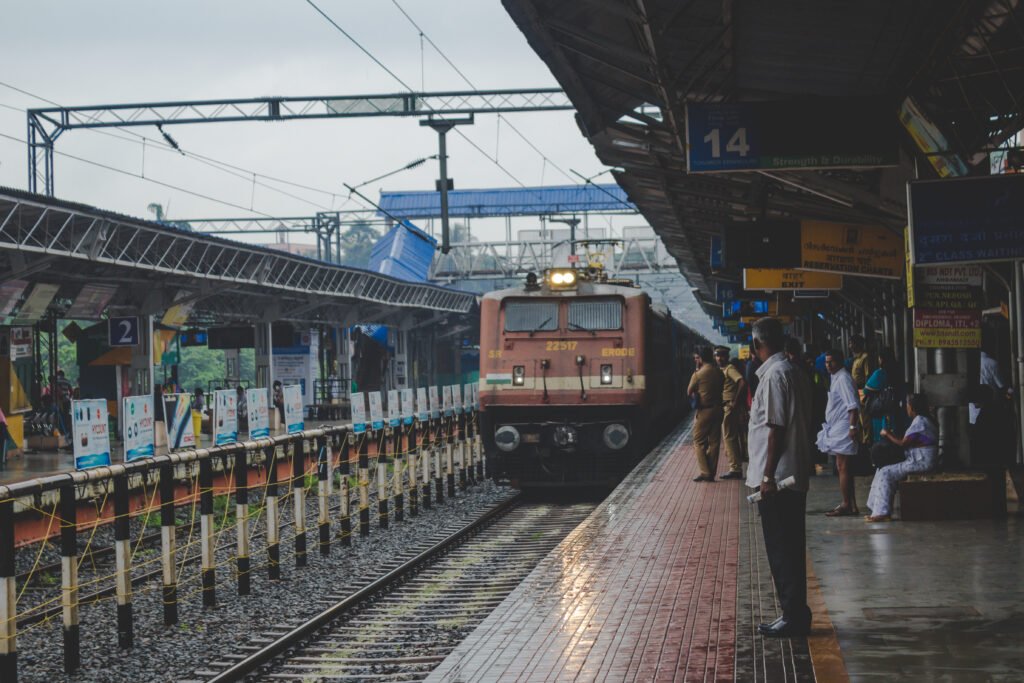 A train arriving at a busy Indian railway station platform with passengers waiting; optimized for land for sale near Tambaram Railway Station.