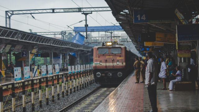 A train arriving at a busy Indian railway station platform with passengers waiting; optimized for land for sale near Tambaram Railway Station.