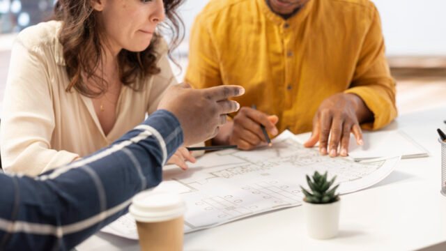 "A diverse group of young professionals sitting at a white desk, reviewing a detailed architectural floor plan and discussing property investment."