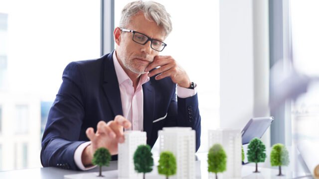 "A real estate investor and a consultant reviewing commercial property lease agreements and a building blueprint in a modern high-rise office."