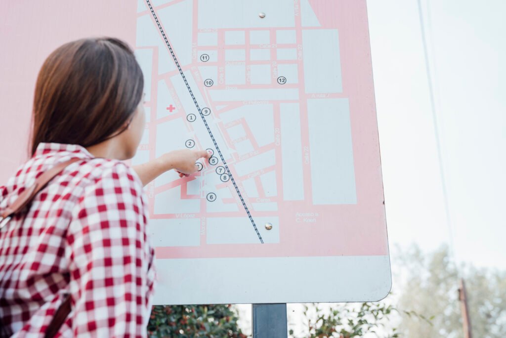 A person in a red checkered shirt pointing at a detailed pink and white layout map on a public signage board, representing a search for plot guideline values in a Chennai neighborhood.