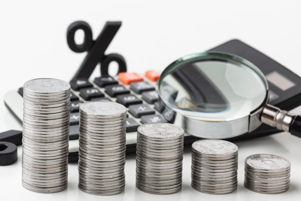 Stacks of coins decreasing in height next to a calculator, magnifying glass, and percentage symbol, illustrating the Loan to Value Ratio.