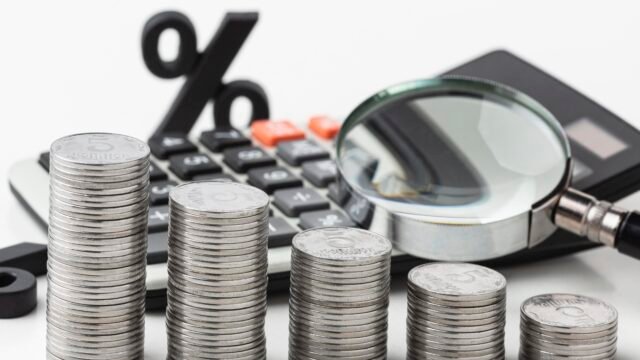 Stacks of coins decreasing in height next to a calculator, magnifying glass, and percentage symbol, illustrating the Loan to Value Ratio.